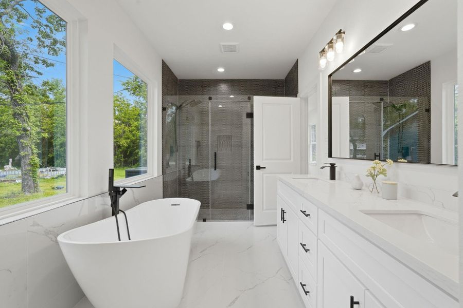 This modern bathroom features a freestanding tub by large windows, a sleek glass-enclosed shower, and a double vanity with ample storage. The bright, airy design is enhanced by natural light and elegant fixtures.
