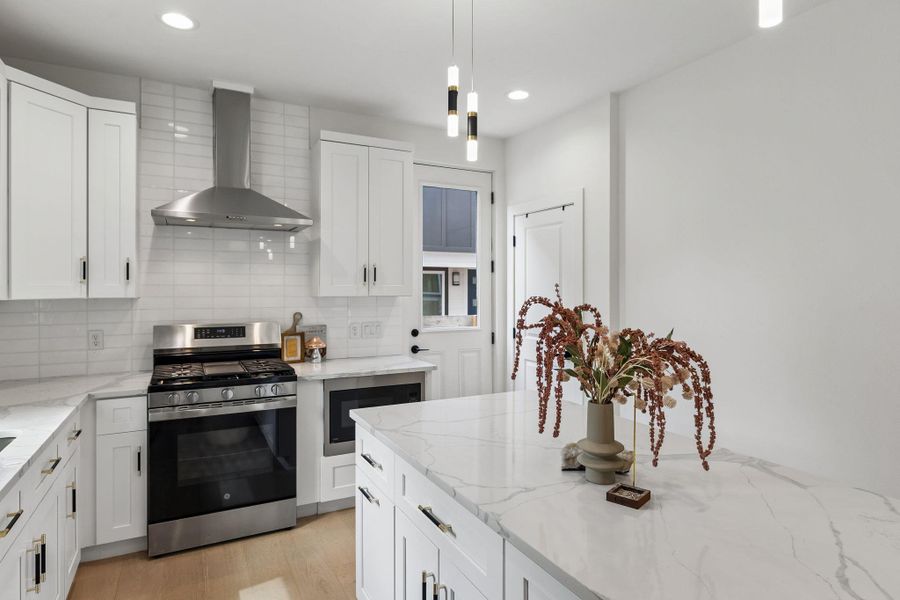 A detailed shot of the quartz island and prep area. The marbling in the stone adds a touch of luxury, while the view highlights the seamless integration of the stainless steel vent hood and white cabinetry.