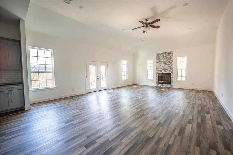 Unfurnished living room with french doors, a stone fireplace, ceiling fan, dark wood-style floors, and vaulted ceiling