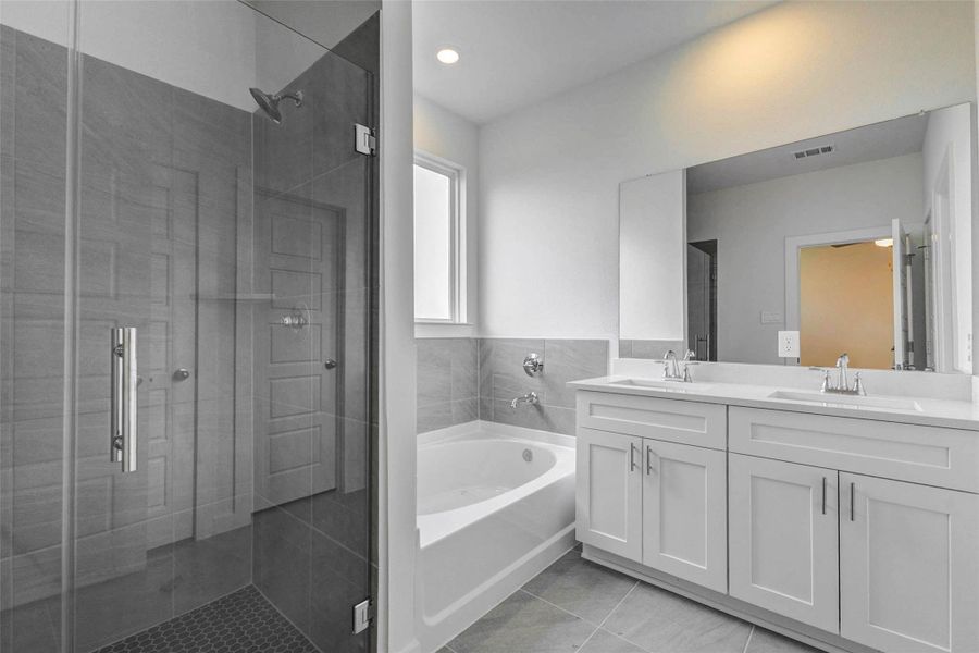 Primary bath with glass-enclosed shower, soaking tub, dual-sink vanity, large mirror, tile flooring, and soft neutral finishes. The layout offers both function and comfort, with separate bathing spaces and a bright, clean design that gives the owner’s suite a spa-inspired feel.