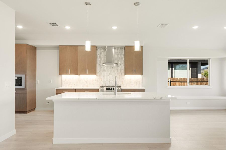 Modern kitchen with large white island, wood cabinets, tile backsplash, and stainless steel range hood