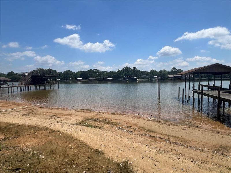 Waterfront property featuring a sandy shoreline, a covered boat dock with wooden decking, an additional uncovered pier, and mature trees lining the distant shore Waterfront property featuring a sandy shoreline, a covered boat dock with wooden decking, an additional uncovered pier, and mature trees lining the distant shore