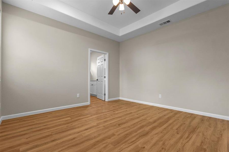 Empty room featuring a tray ceiling, light wood finished floors, and a ceiling fan