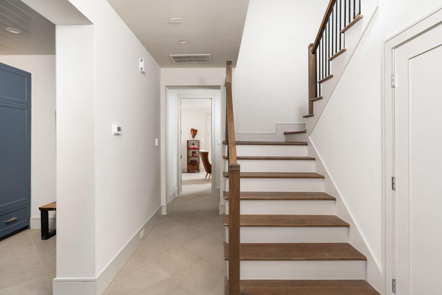 The hallway to the first floor bedroom shows off the large-format tile, deep baseboards, and stained oak stair treads. The hallway to the first floor bedroom shows off the large-format tile, deep baseboards, and stained oak stair treads.