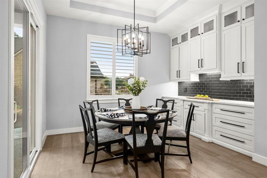 Quaint kitchen dining with tray ceiling and crown molding, beautiful light fixture, custom built-in cabinetry and access to large, back patio