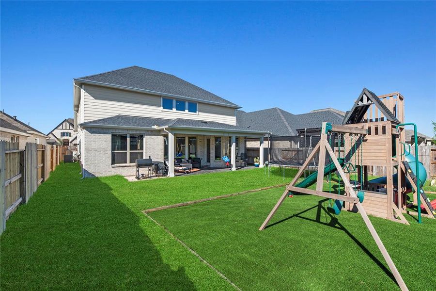 This photo showcases a spacious backyard with a well-maintained lawn and a children's playset. The two-story home features a covered patio area, providing an ideal outdoor living space for relaxation and entertainment.