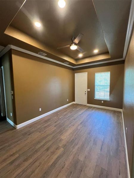 Empty room featuring a tray ceiling, wood finished floors, and ceiling fan Empty room featuring a tray ceiling, wood finished floors, and ceiling fan
