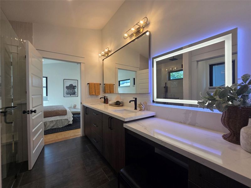 A contemporary primary bathroom features dark tile flooring, stone countertops, and sleek minimalist cabinetry.