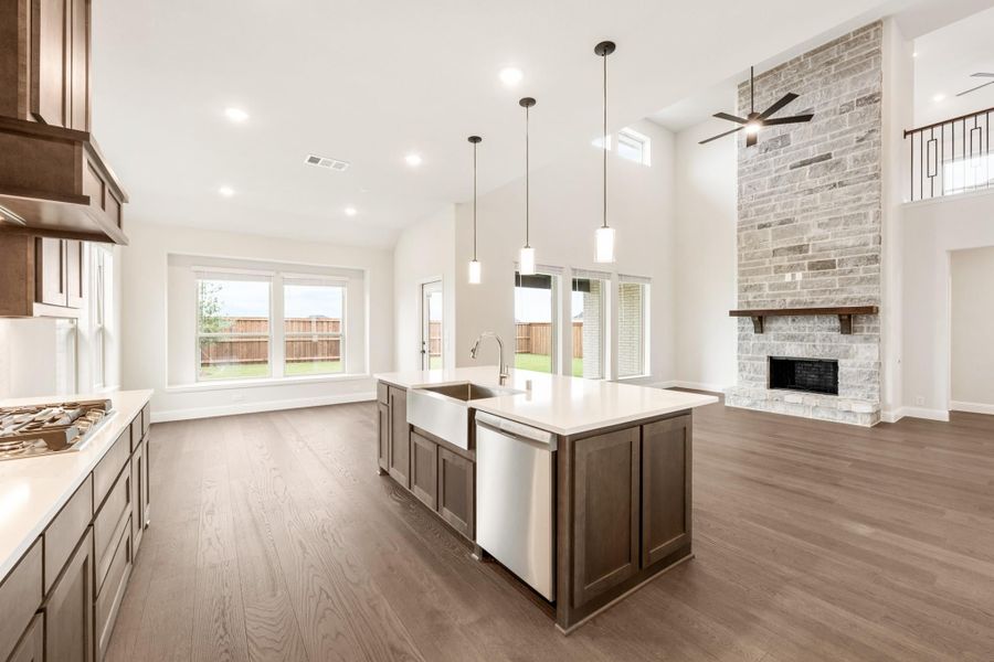 Open-concept kitchen with large island, farmhouse sink, and stone fireplace in adjoining living area with high ceilings and hardwood floors