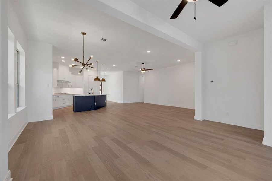 Unfurnished living room with ceiling fan, hanging lights, and light wood-type flooring