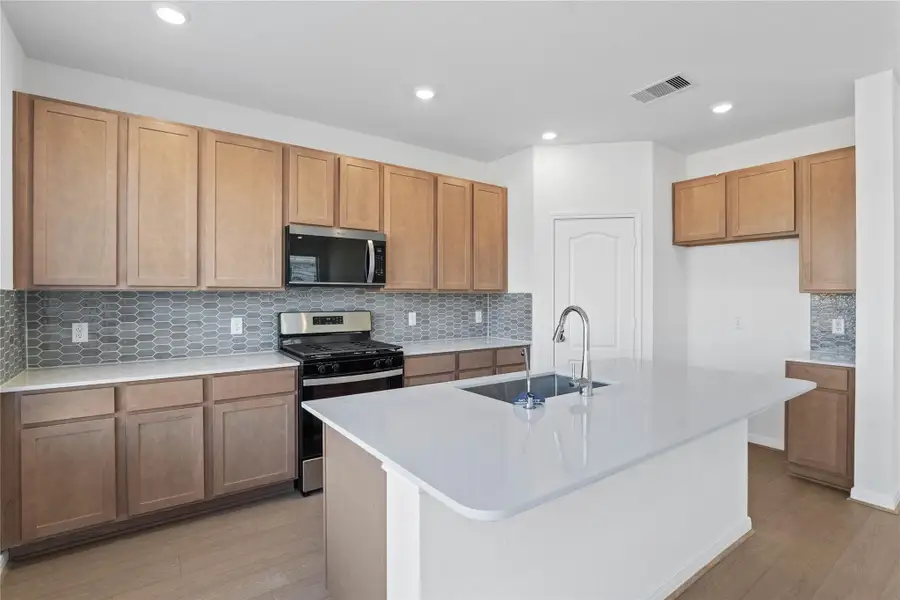 This spacious kitchen boasts soaring ceilings, Woodmont Dakota cabinets in a Barley stain, Silestone Miami White countertops, stainless steel Whirlpool appliances, a modern Daltile backsplash, recessed lighting, an extended breakfast bar countertop to the kitchen island, and a pantry—all overlooking the expansive family room. This spacious kitchen boasts soaring ceilings, Woodmont Dakota cabinets in a Barley stain, Silestone Miami White countertops, stainless steel Whirlpool appliances, a modern Daltile backsplash, recessed lighting, an extended breakfast bar countertop to the kitchen island, and a pantry—all overlooking the expansive family room.