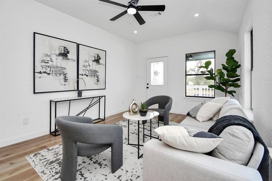 This is a modern kitchen featuring white cabinetry, stainless steel appliances, a dark countertop, and light wood flooring. There are two doors, possibly a pantry and an exit, and a window that allows for natural light.