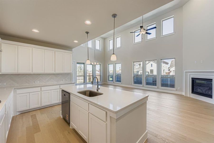 Kitchen with white cabinets, decorative backsplash, light wood-type flooring, a glass covered fireplace, and pendant lighting