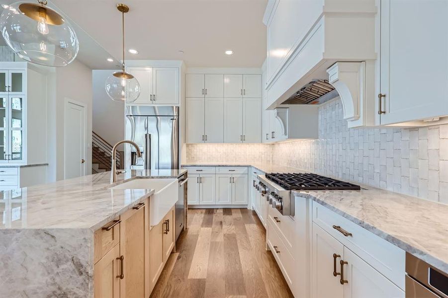 Kitchen with an island with sink, stainless steel appliances, light stone countertops, and light hardwood / wood-style floors