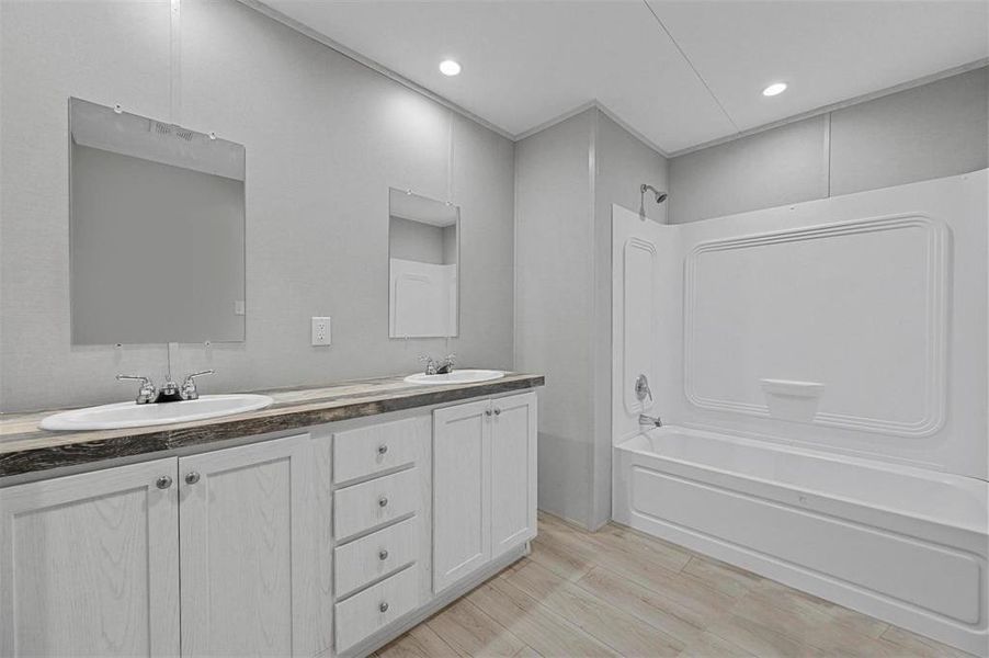 Bathroom with shower / tub combination, wood finished floors, double vanity, and a sink