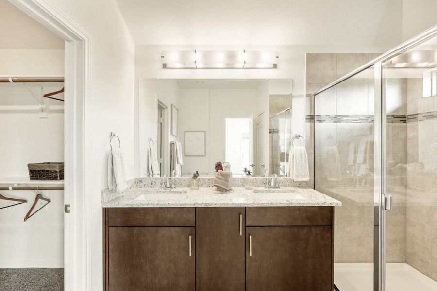Bathroom with double sink vanity, dark wood cabinets, granite countertop, glass shower, and walk-in closet entrance