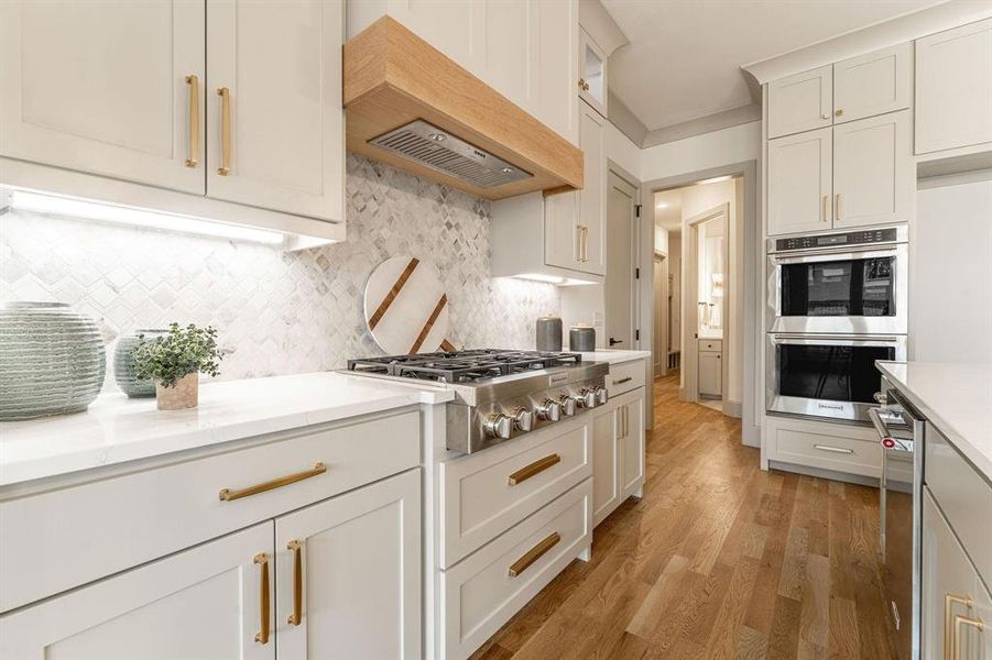 Kitchen with stainless steel appliances, light wood-type flooring, light stone counters, and white cabinets