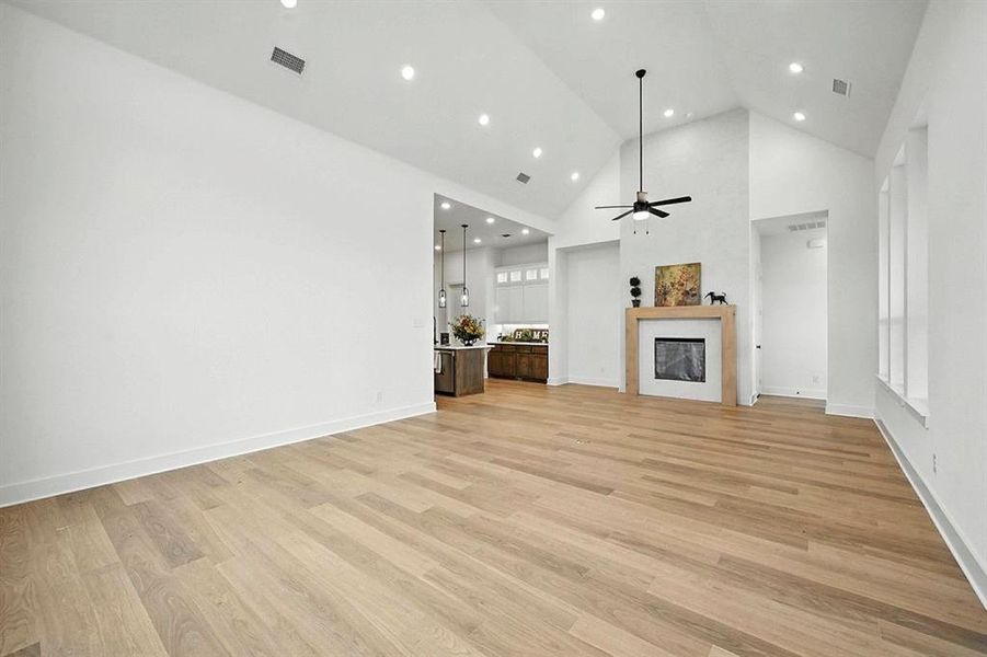 Unfurnished living room featuring a fireplace, high vaulted ceiling, light wood finished floors, a ceiling fan, and recessed lighting