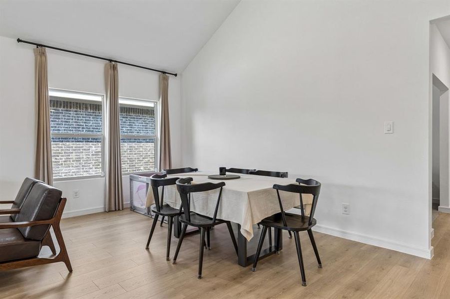 Living area featuring vaulted ceilings, light wood-style flooring, and two windows with blinds