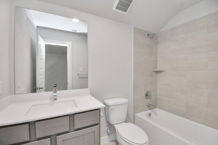 Secondary bath features tile flooring, bath/shower combo with tile surround, light stained wood cabinets, beautiful light countertop.