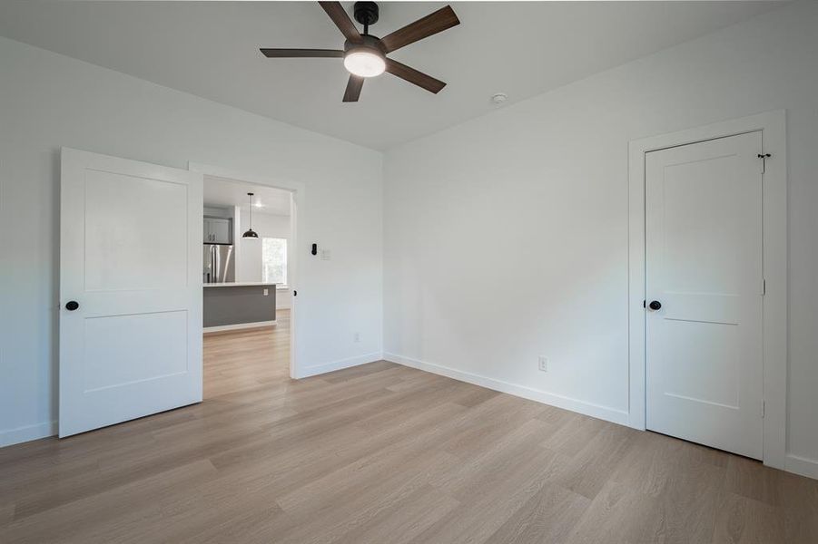 Unfurnished bedroom featuring stainless steel refrigerator with ice dispenser, light wood finished floors, and ceiling fan Unfurnished bedroom featuring stainless steel refrigerator with ice dispenser, light wood finished floors, and ceiling fan