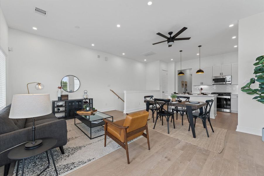 Perched on the second floor, this open-concept living, dining, and kitchen area flows effortlessly beneath high ceilings and across rich engineered hardwood floors that unify the space with warmth and elegance. A set of French doors anchors the room, inviting natural light and offering a glimpse of downtown through the balcony beyond. The layout encourages seamless entertaining and everyday comfort, with each zone connected yet distinct, framed by clean lines and contemporary finishes.