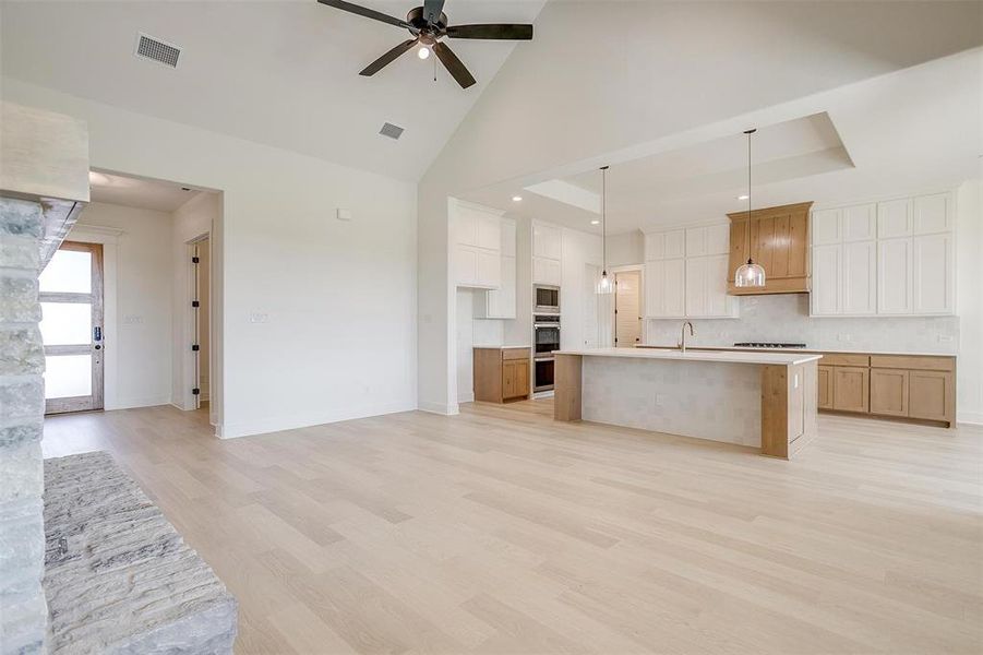 Kitchen with a center island with sink, sink, decorative light fixtures, white cabinets, and light hardwood / wood-style floors