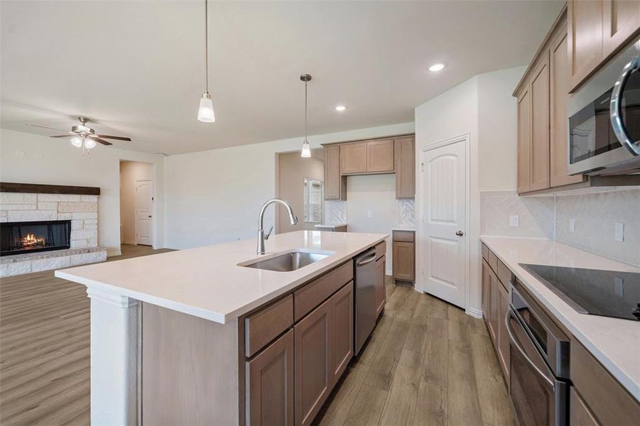 Kitchen featuring light wood-style floors, hanging light fixtures, decorative backsplash, open floor plan, and light stone counters
