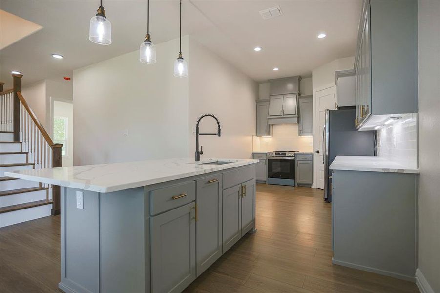 Kitchen featuring a kitchen island with sink, sink, dark hardwood / wood-style flooring, appliances with stainless steel finishes, and decorative light fixtures