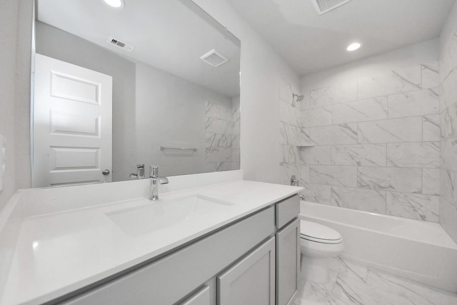 Secondary bath features tile flooring, bath/shower combo with tile surround, light stained wood cabinets, beautiful light countertop. Sample photo of completed home with similar floor plan. Actual colors and selections may vary.
