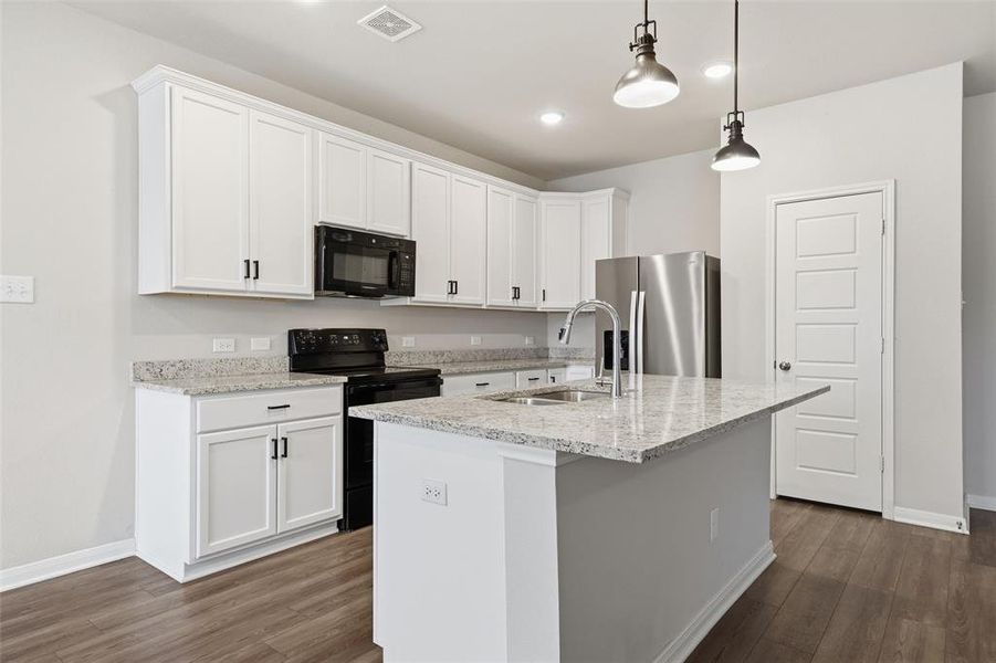 Kitchen with black appliances, hanging light fixtures, white cabinets, a kitchen island with sink, and light stone counters