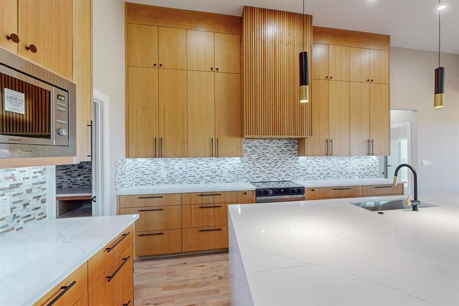 Kitchen featuring appliances with stainless steel finishes, sink, backsplash, hanging light fixtures, and light hardwood / wood-style floors