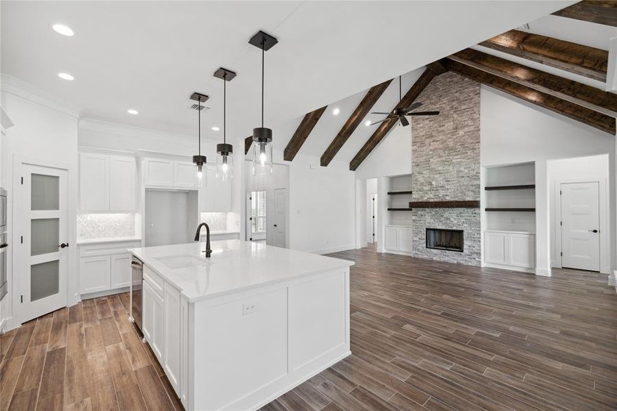 Kitchen featuring white cabinets, a fireplace, sink, beam ceiling, and an island with sink