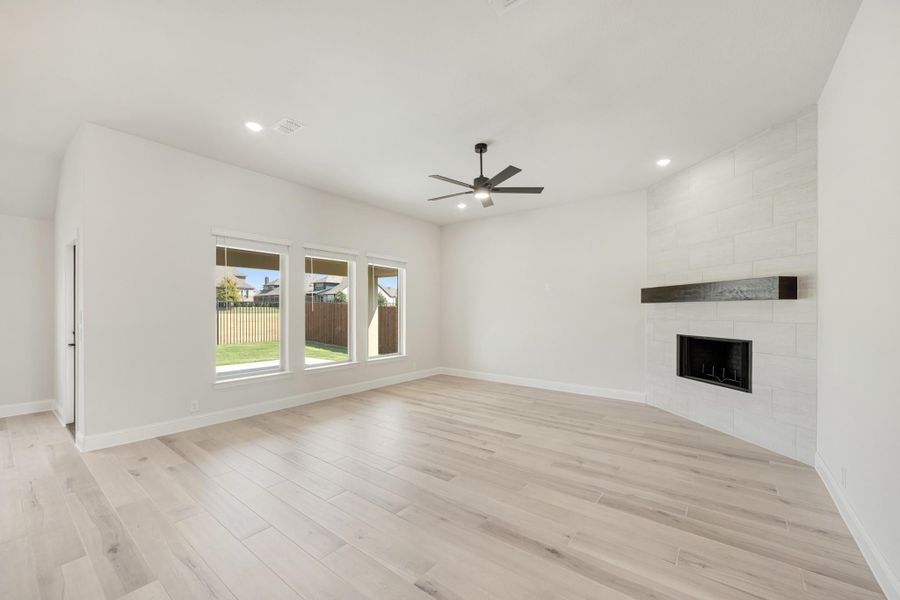 Open living room with light wood floors, ceiling fan, and tile-surround fireplace with wood mantel