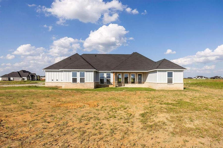 Rear view of house with board and batten siding, a shingled roof, brick siding, and a yard Rear view of house with board and batten siding, a shingled roof, brick siding, and a yard