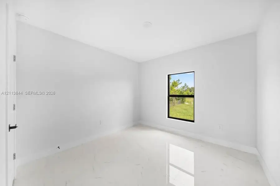 Interior space featuring polished white tile flooring with grey veining, crisp neutral wall paint, and a single-pane window with a black frame Interior space featuring polished white tile flooring with grey veining, crisp neutral wall paint, and a single-pane window with a black frame