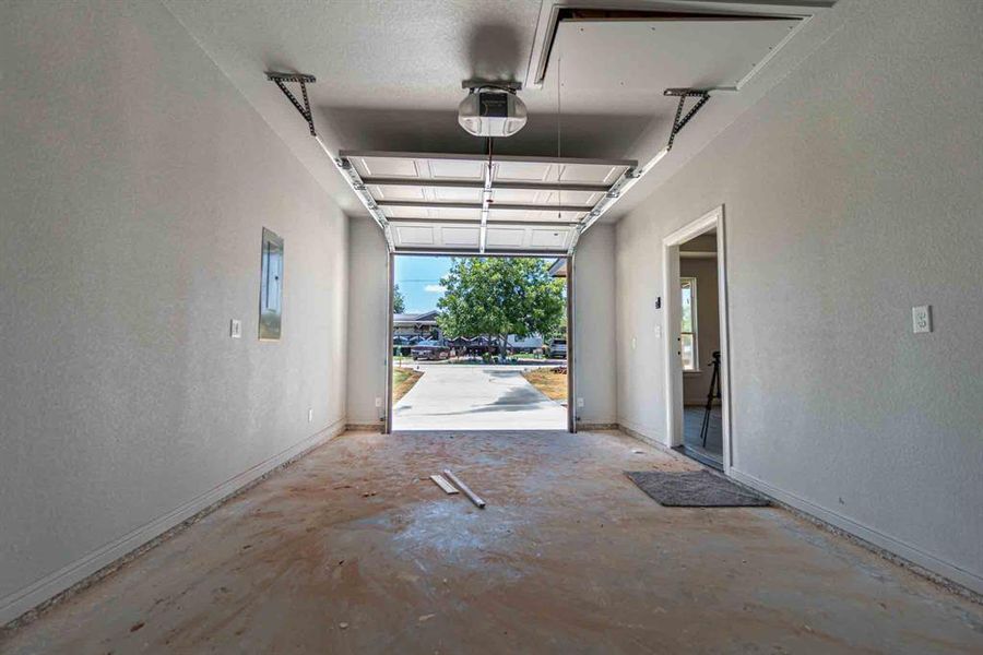 Garage with a textured wall, a garage door opener, and electric panel Garage with a textured wall, a garage door opener, and electric panel