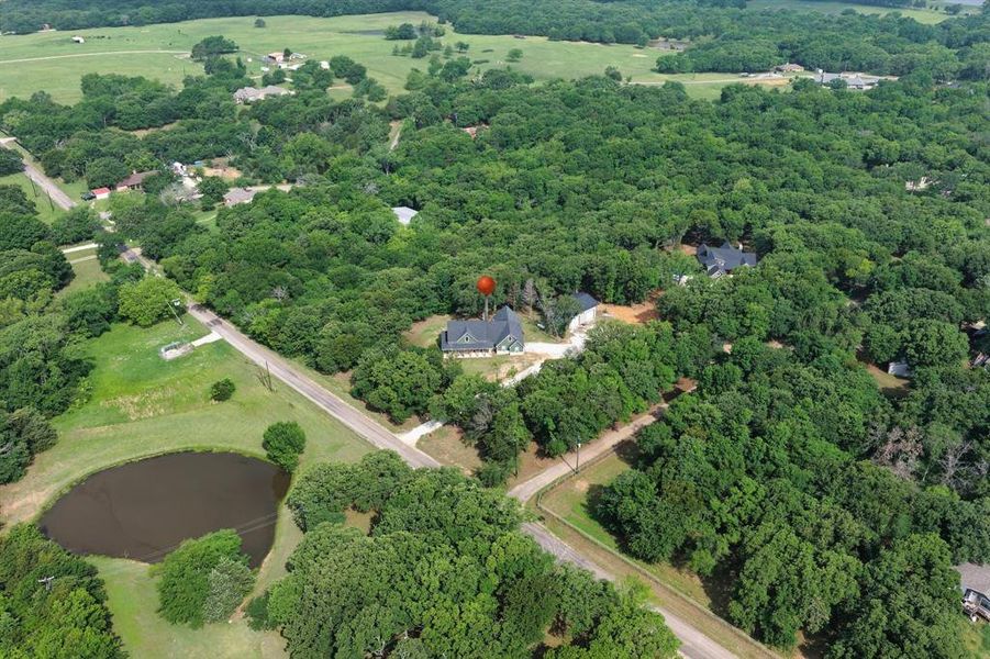 Aerial overview of a property surrounded by mature trees, featuring a visible pond and extensive green landscape