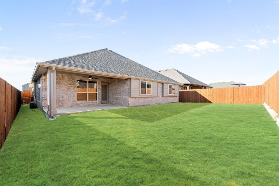 Backyard of single-story brick home with covered patio, green lawn, and wood privacy fence. Backyard of single-story brick home with covered patio, green lawn, and wood privacy fence.