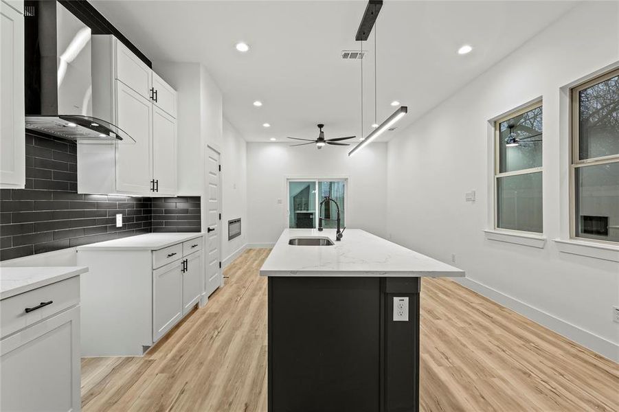 Kitchen with sink, white cabinetry, wall chimney exhaust hood, and an island with sink