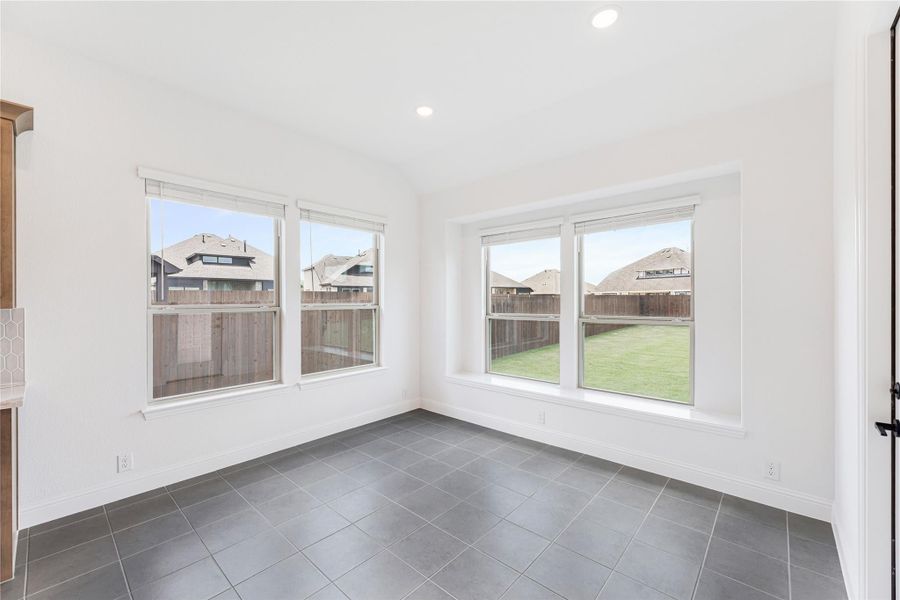 Empty room with gray tile floors, white walls, and large windows overlooking a fenced backyard