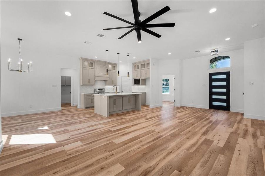 Unfurnished living room featuring ceiling fan with notable chandelier, light wood-type flooring, and sink