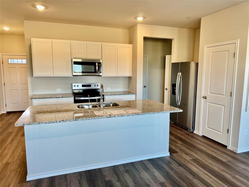 Kitchen with stainless steel appliances, light stone countertops, white cabinetry, dark wood-type flooring, and a center island with sink Kitchen with stainless steel appliances, light stone countertops, white cabinetry, dark wood-type flooring, and a center island with sink
