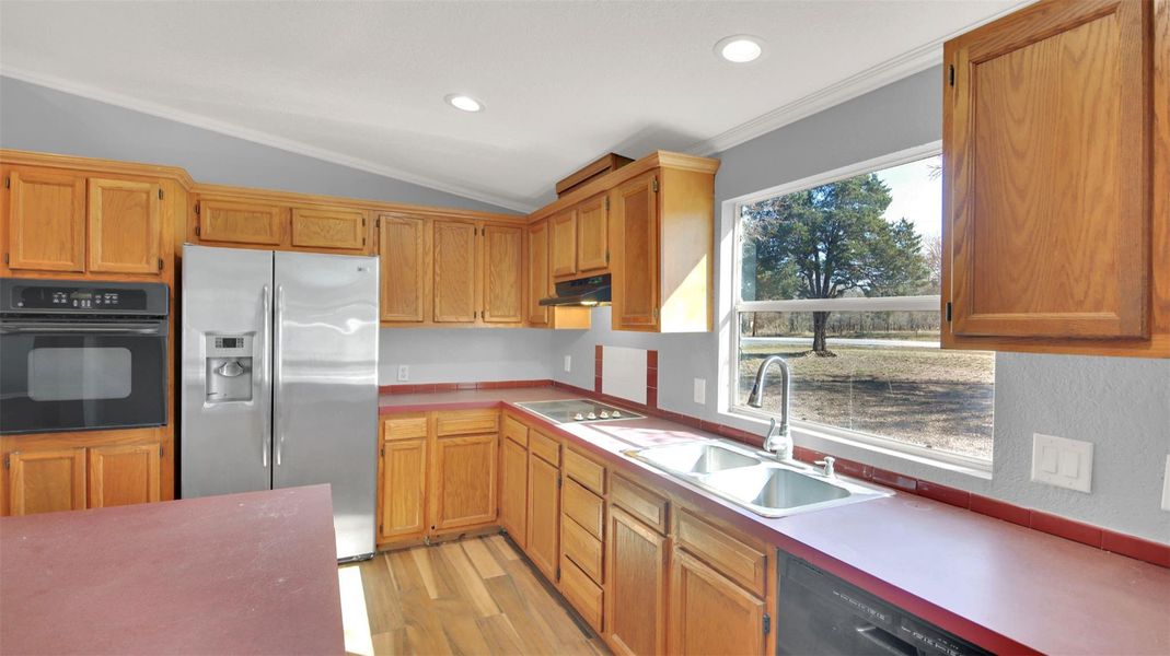 Kitchen featuring black appliances, light wood-style floors, lofted ceiling, recessed lighting, and brown cabinets