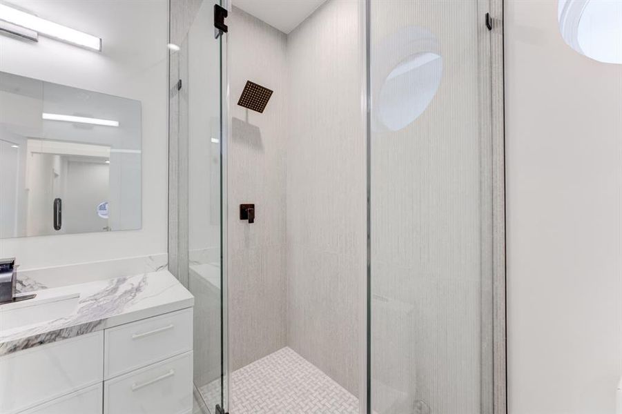 Frameless glass shower door with black hardware and neutral toned tile.