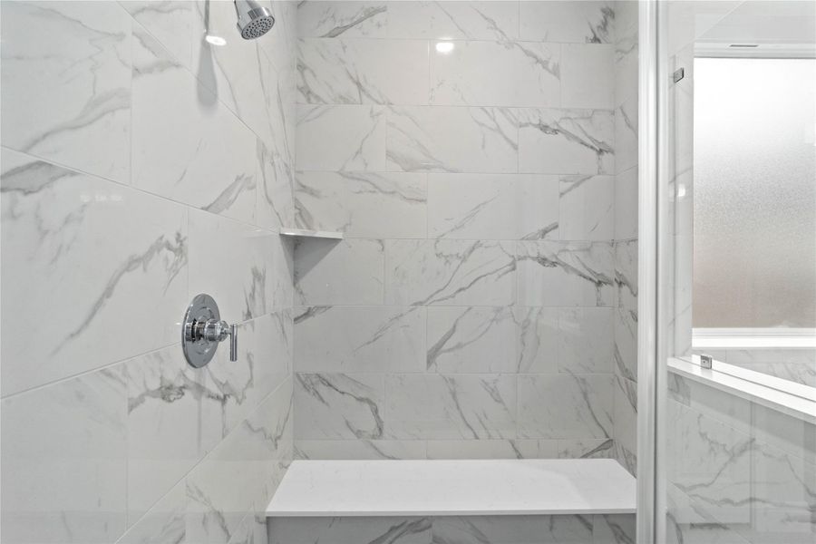 The walk-in shower includes a convenient, integrated bench with a niche shelf, offering comfort, extra storage space, and a high-end, custom appearance.