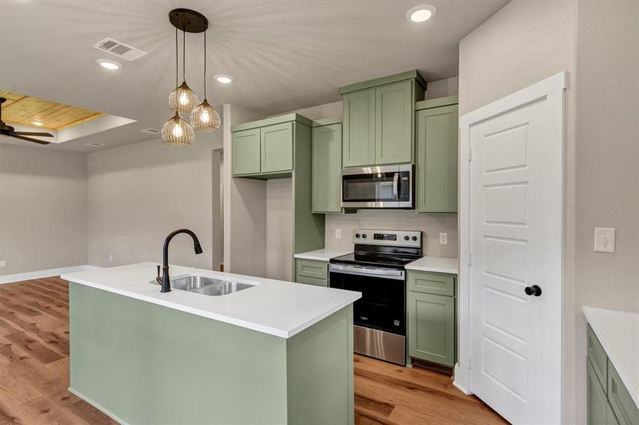Kitchen featuring green cabinetry, stainless steel appliances, light wood-style floors, recessed lighting, and decorative light fixtures Kitchen featuring green cabinetry, stainless steel appliances, light wood-style floors, recessed lighting, and decorative light fixtures