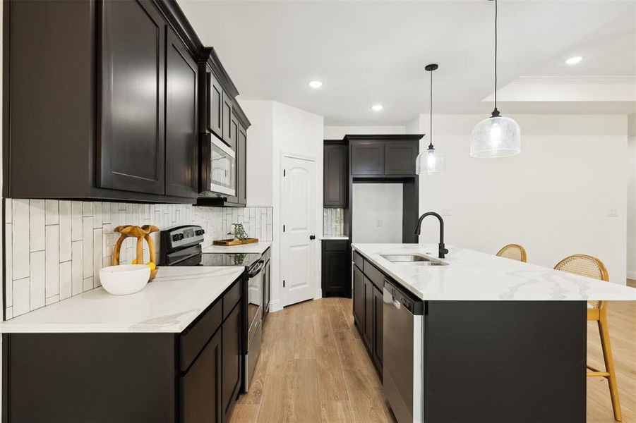 Kitchen featuring stainless steel appliances, pendant lighting, decorative backsplash, sink, and light hardwood / wood-style flooring