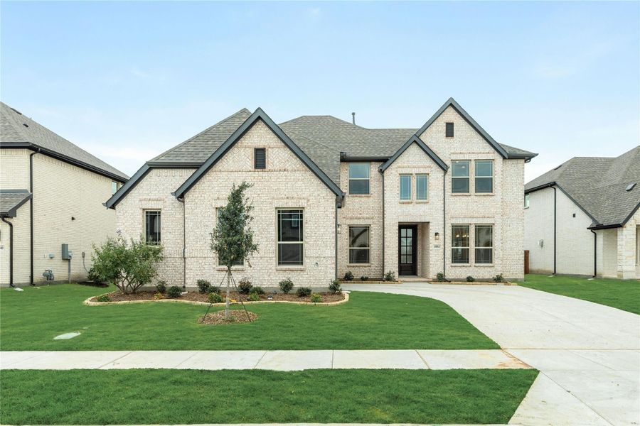 Two-story white brick home with dark roof, manicured front lawn, and concrete driveway