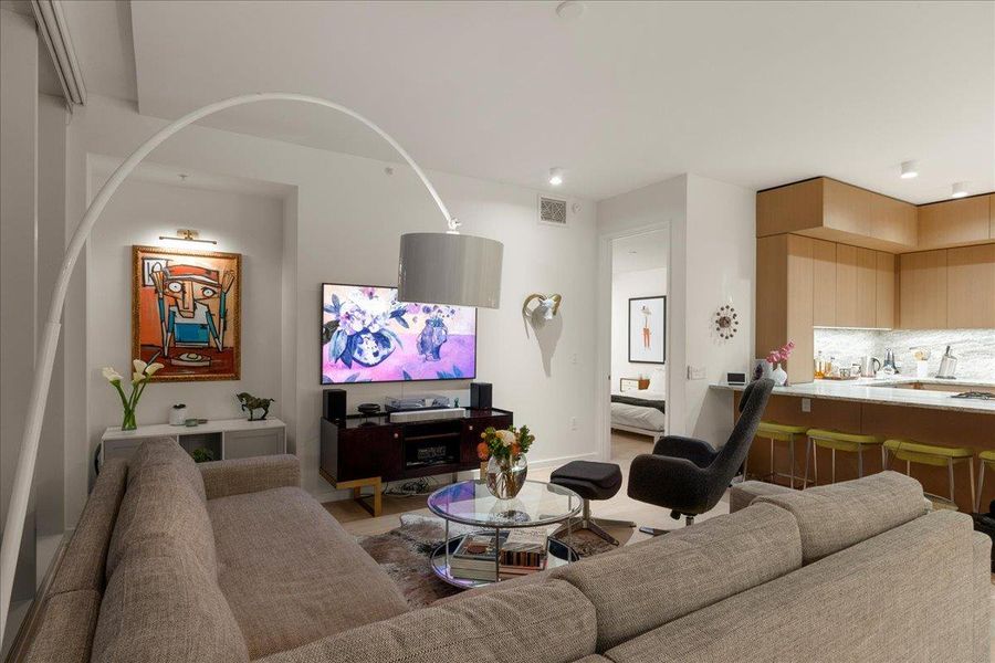 Inviting living room with open flow to the kitchen and dining, featuring floor-to-ceiling windows, custom shades, and space designed for both relaxation and entertaining.